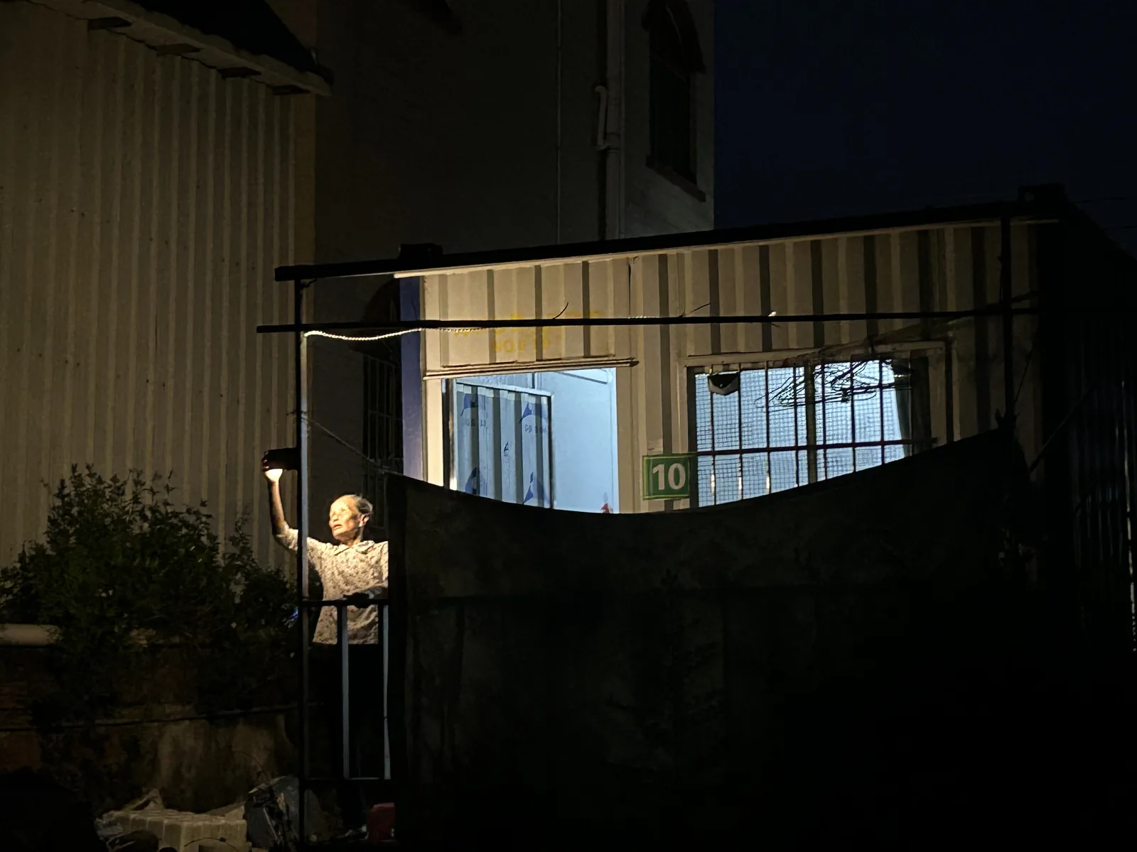 长者在夜间举起新安装的感应灯查看屋外环境